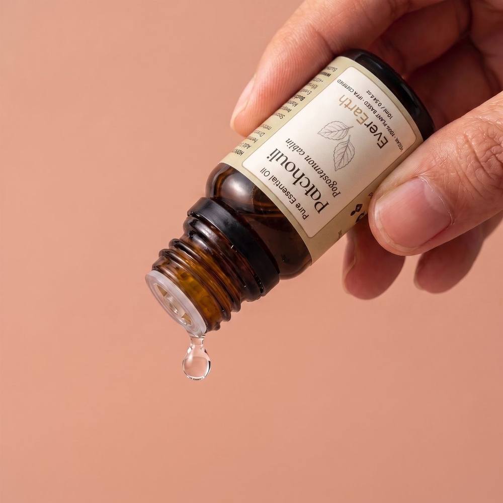 Hand dispensing a drop of EverEarth Patchouli essential oil from the amber glass bottle